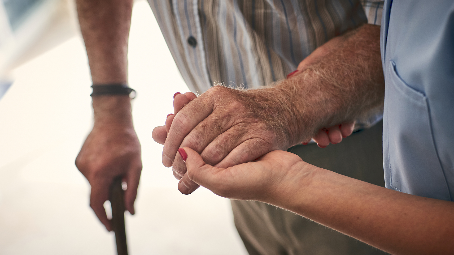 A healthcare provider leading an elderly man with a cane.